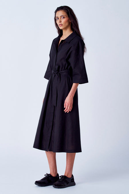 Robe noire à manches courtes de YŪGEN, avec une ceinture à la taille et des chaussures noires.
