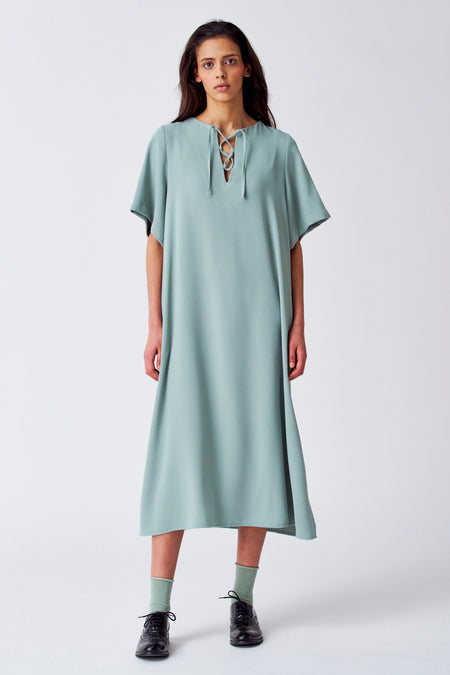 Robe verte avec manches courtes de YŪGEN, avec un détail vétérinaire au col et des chaussettes vertes visibles avec des chaussures noires.
