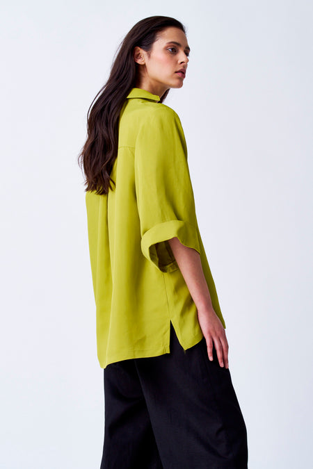 Blouse jaune de YŪGEN avec des manches trois-quarts, associée à un pantalon noir et un fond uni.