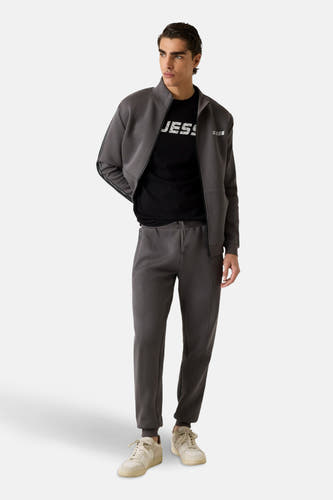 Gilet gris de Guess, porté sur un t-shirt noir, associé à des pantalons coordonnés et des baskets blanches.