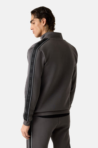 Grijs vest van Guess® met een hoge halslijn en een zwart logopatroon langs de mouwen.
