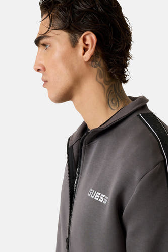 Gilet gris de Guess avec fermeture éclair et logo blanc, détail sur l'épaule et le cou tatoué.