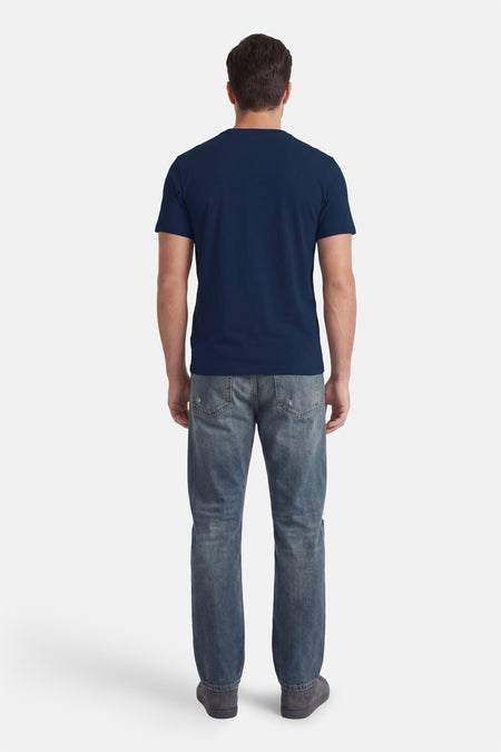T-shirt bleu à manches courtes de Guess®, vu de dos, combiné avec un jean et des chaussures gris foncé.