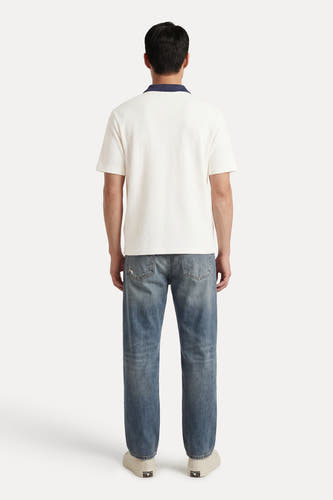 Polo écru à manches courtes de Guess®, avec une texture piquée, portée avec un jean et des baskets blanches, vue de dos.