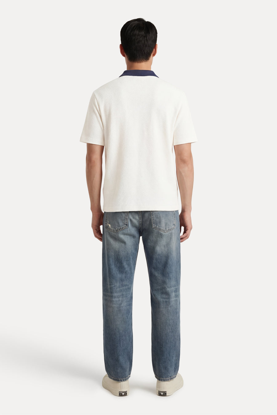 Polo écru à manches courtes de Guess®, avec une texture piquée, portée avec un jean et des baskets blanches, vue de dos.