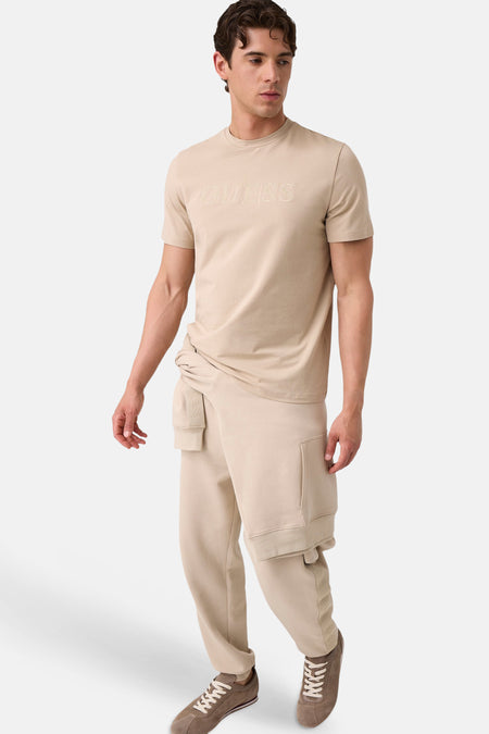 Beige korte mouwen T-shirt met geborduurd Guess-logo, van Guess, gedragen met beige joggingbroek en bruine sneakers, front view