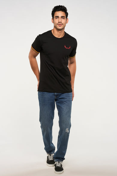 T-shirt noir de ZEB STYLE LAB, avec manches courtes et imprimé rouge "DEVILS", combiné avec un jean bleu et des baskets noires.