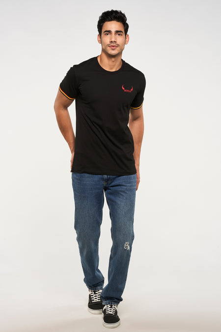 T-shirt noir de ZEB STYLE LAB, avec manches courtes et imprimé rouge "DEVILS", combiné avec un jean bleu et des baskets noires.