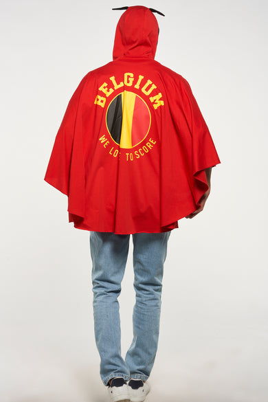 Poncho rouge de ZEB STYLE LAB, avec drapeau belge et texte au dos, porté avec un jean et des baskets blanches.